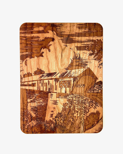 Wooden cutting board with engraved design of a covered bridge over water