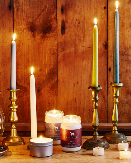 a tabletop filled with various candlesticks, oil lamps, tea light candles, and jar candles all giving off a warm glow