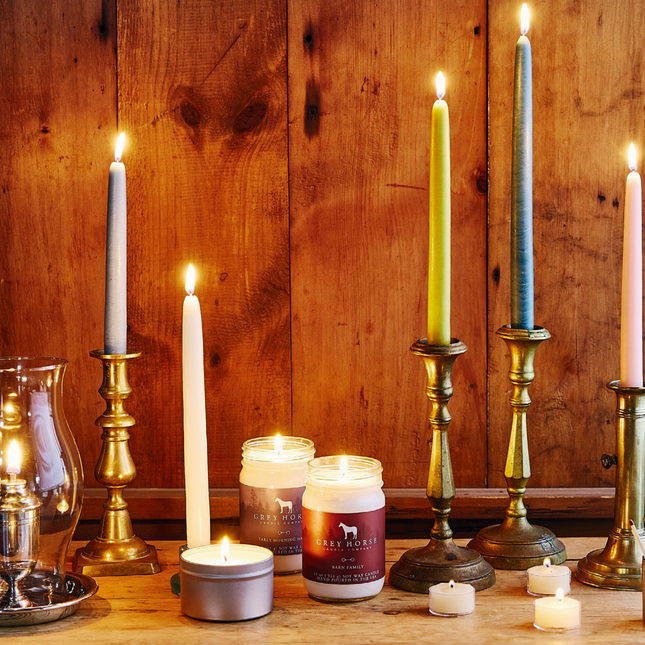 a tabletop filled with various candlesticks, oil lamps, tea light candles, and jar candles all giving off a warm glow