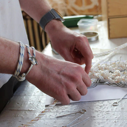 a white with blue stripes wrap bracelet with silver anchor charm on a model who is hand tying knots