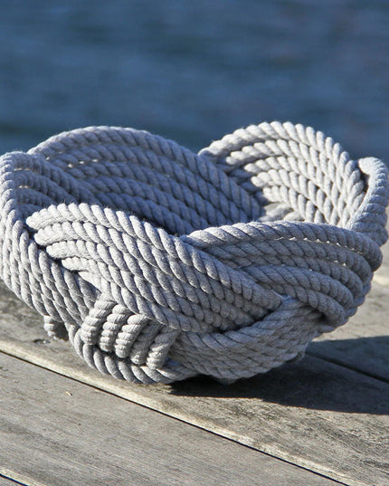 a hand woven cotton rope bowl in gray resting on a dock with a view of the water