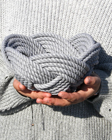 a hand woven cotton rope bowl in gray as seen in the hands of someone holding it about chest high showing that it is slightly wider than two hands loosely clasped together