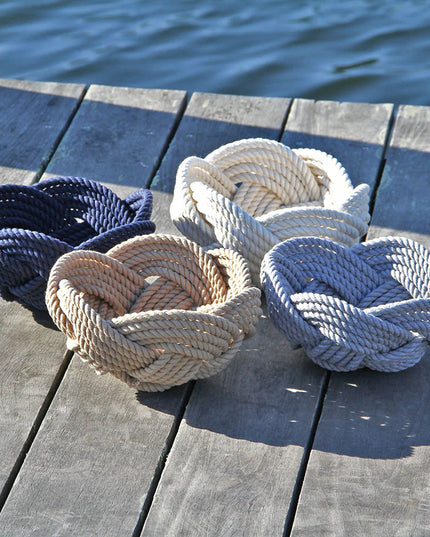 a collection of all of the colors of hand woven celtic knot rope bowls on a dock: navy, tan, white, and gray