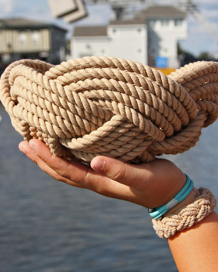 a hand woven cotton rope bowl in tan as seen in profile being held up by one single hand showing the scale of the bowl