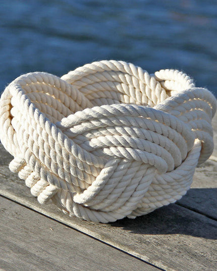 a hand woven cotton rope bowl in white resting on a dock with a view of the water