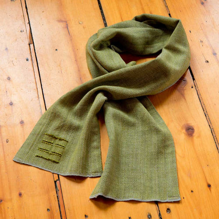 the camden scarf in tarragon (green) on a wooden surface