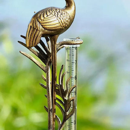 detail view of the crane rain gauge in a garden, featuring the elegant details of the crane, sculpted fronds, and clear rain gauge with markings to measure rainfall