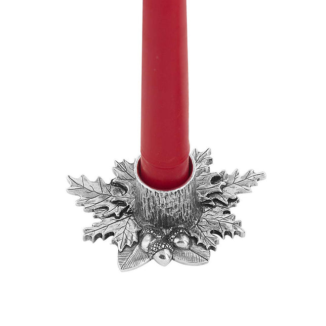 close up view of a detailed candleholder with autumnal leaf shapes and acorns surrounding the base of the candle holder and holding a red candle
