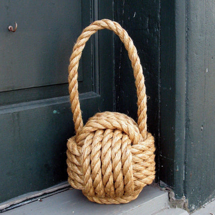 a large monkey fist knot door stop made of manila rope leaning against a dark green door