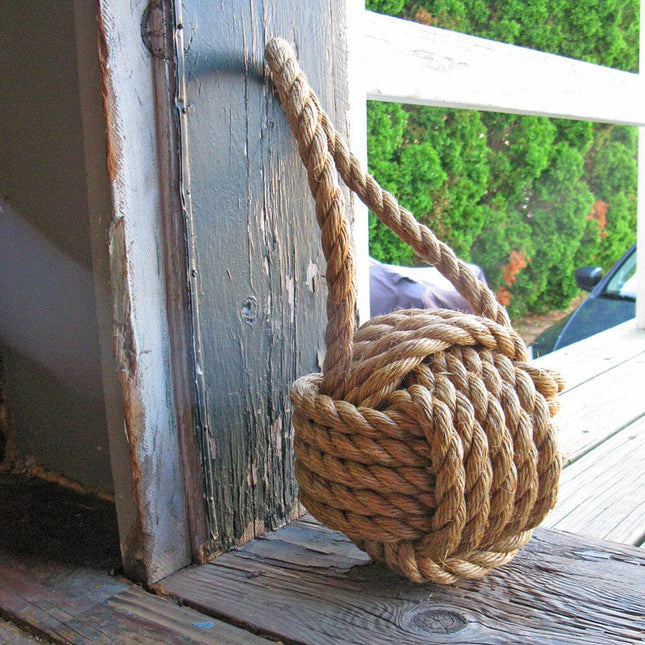 a large monkey fist knot door stop  made of manila rope leaning against a doorway
