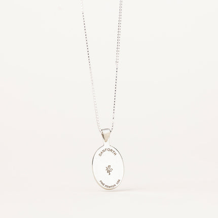 the back of the pewter pendant showing the maker's mark stamped on it, hanging from a silver chain