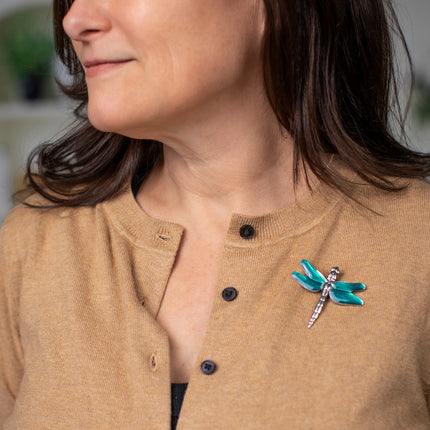 a model wearing a camel-colored sweater adorned with the dragonfly brooch