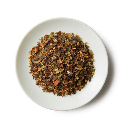a small white round dish containing a mound of emerald honeybush loose leaf tea showing the honeybush and seaweed ingredients
