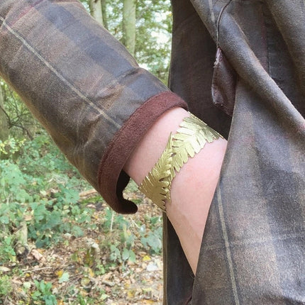 the fern cuff on a model's wrist with hand in pocket, model is wearing a green and brown plaid coat and standing in a forest