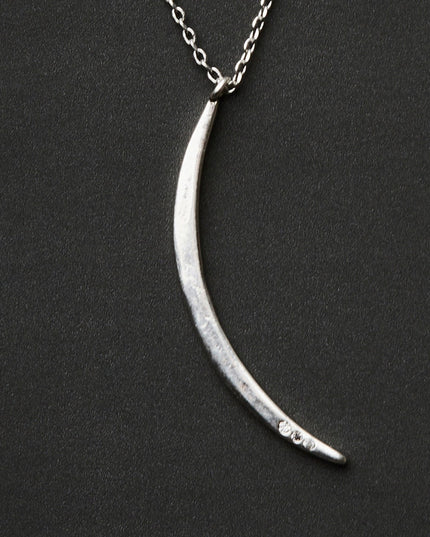 a slender silver pendant in the shape of a slice of the moon in its gibbous phase with 3 mini CZ stones on the bottom curve