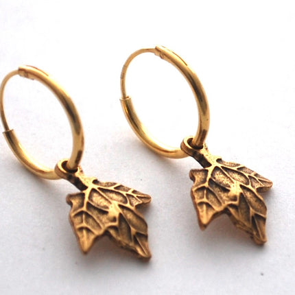 close up of gold maple hoop earrings on a white surface