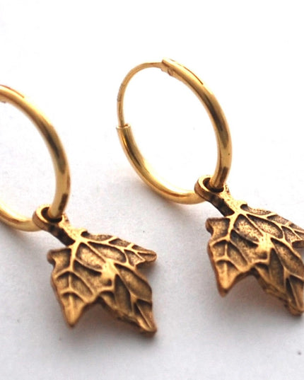 close up of gold maple hoop earrings on a white surface