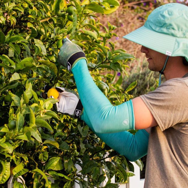a model tending to a shrub while wearing the heather green protection sleeves
