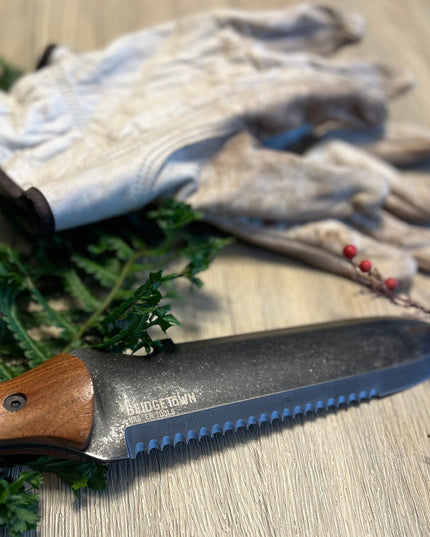 Essential Hori Hori knife unsheathed on a surface alongside some freshly cut greens with gardening gloves