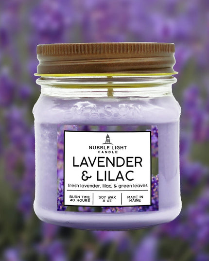 a candle in a clear glass mason jar with light purple wax and a label that reads "Lilac & Lavender" against a soft image of a lavender field