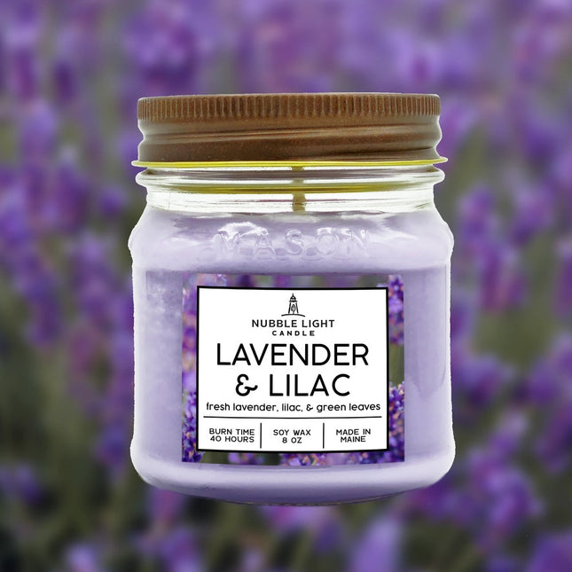 a candle in a clear glass mason jar with light purple wax and a label that reads "Lilac & Lavender" against a soft image of a lavender field