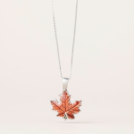 a maple leaf shaped pendant in brilliant orange with lovely leaf details hanging from a silver chain