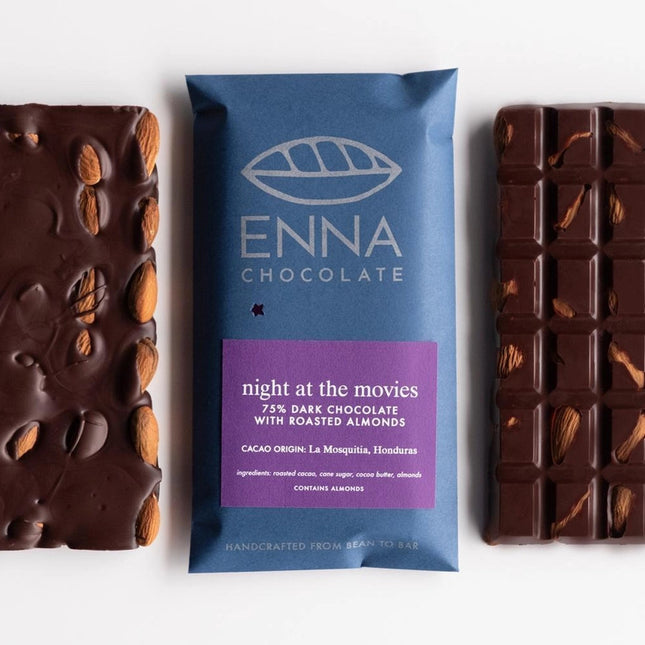 three Night at the Movies bars side by side - two unwrapped bars with a wrapped one in the center. Rich dark chocolate is pebbled with whole almonds, the chocolate bar wrapper is royal blue with a purple label with product info