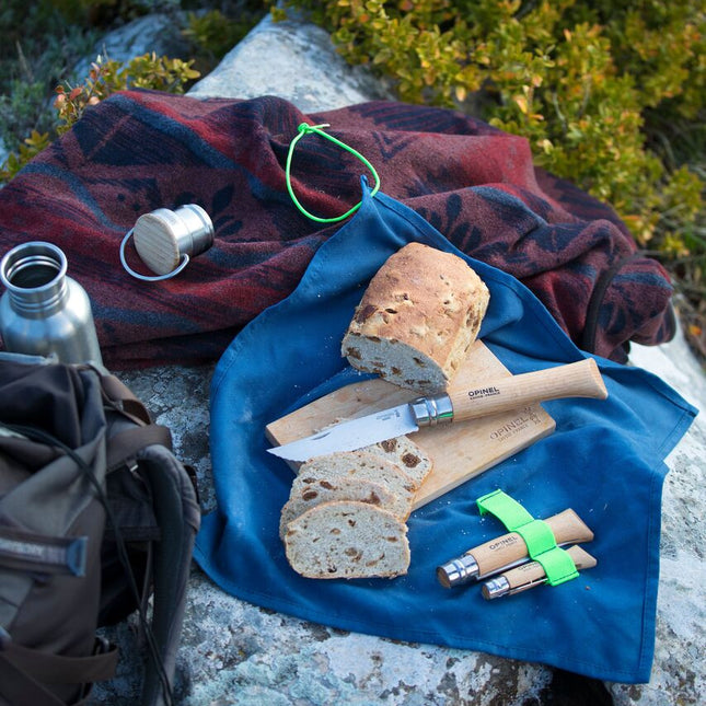 the Nomad Cooking kit with a loaf of bread on the cutting board laid out on a rock alongside other camping gear