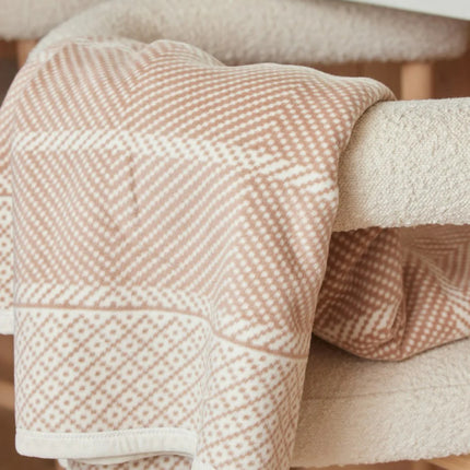 An Old Port Herringbone Tan blanket draped over the arm of a chair