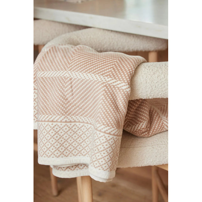 An Old Port Herringbone Tan blanket draped over the arm of a chair