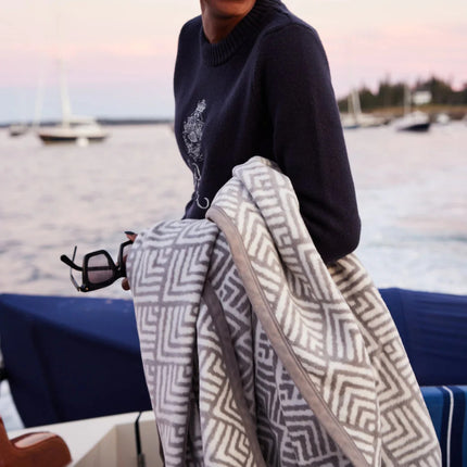 a smiling model on a boat with the blanket draped over her arm, in the background the sea and other sailboats are visible