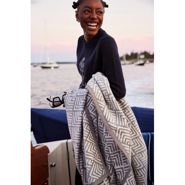 a smiling model on a boat with the blanket draped over her arm, in the background the sea and other sailboats are visible