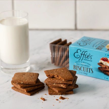 a marble countertop with a glass of milk next to an open box of effie's pecan biscuits stacked and ready to be dunked into milk