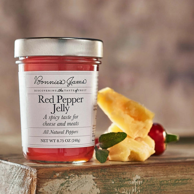 Bonnie's Raspberry Lime Rickey jam jar with an elegant white label and silver jar top on a table next to cheese, herbs, and a red pepper