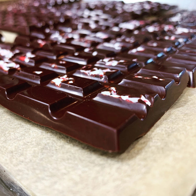 a production table with peppermint bark bars before packaging - rich bars of dark chocolate speckled with white and red candy line the table