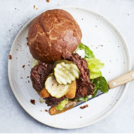 a hamburger on a plate with the top bun off to the side to reveal the pickles topping the burger