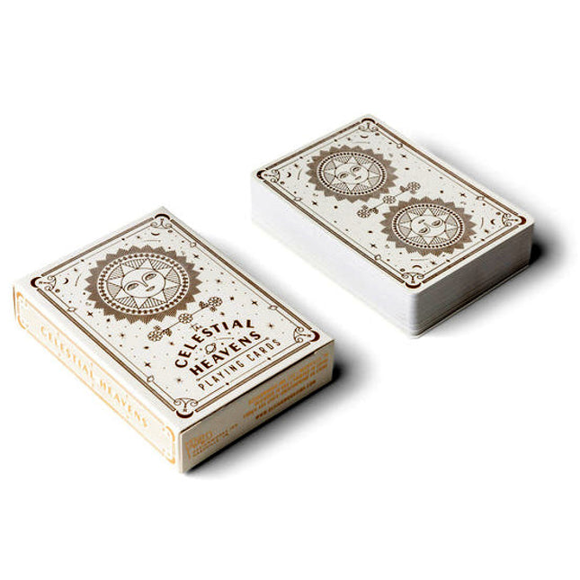 The celestial heavens playing cards deck and box side by side with celestial artwork that includes two radiant suns with faces, surrounded by minimalistic stars, crescent moons, and tiny planets