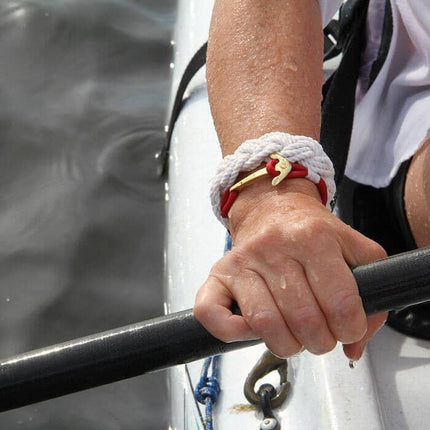 closeup of an arm with a sailor bracelet on the wrist, the hand is holding an oar with a boat and water beneath it