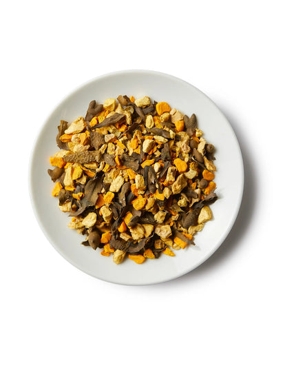 a small white round dish containing a mound of sailor's cure all loose leaf tea showing the strong yellow turmeric ingredients, seaweed, and others