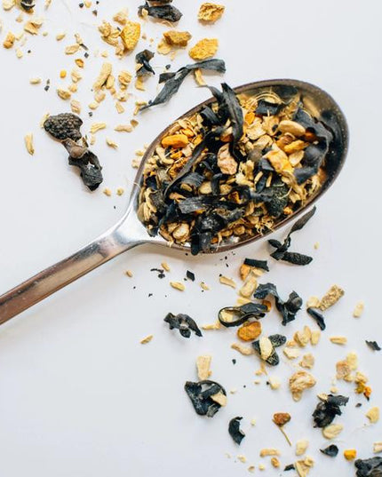 a silver spoon with a heap of sailor's cure all loose leaf tea on a white surface with a diagonal band of loose leaf tea sprinkled across it