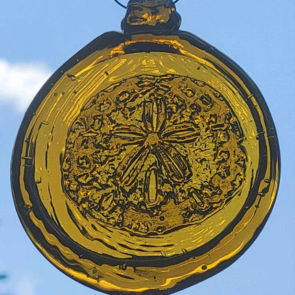 a round amber yellow glass sun catcher with relief image of a sand dollar