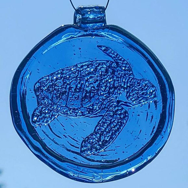 a round blue glass sun catcher with relief image of a sea turtle