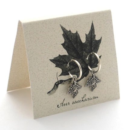 silver maple hoop earrings on an off white backer card printed with a black and gray illustration of a maple leaf