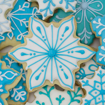 Icy Snowflake shaped cookie with white icing with blue piped snowflake detailed decor atop a pile of other blue and white decorated snowflake cookies