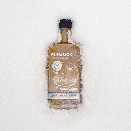 snow globe maple syrup bottle resting atop a blanket of snow to show the wintry magic of this syrup