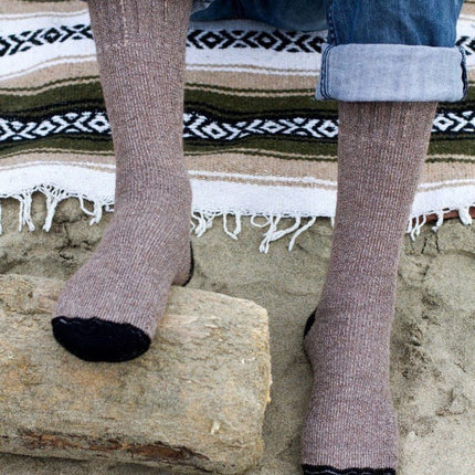 close up of a pair of feet wearing the cocoa brown alpaca adventure socks on a striped blanket on the beach