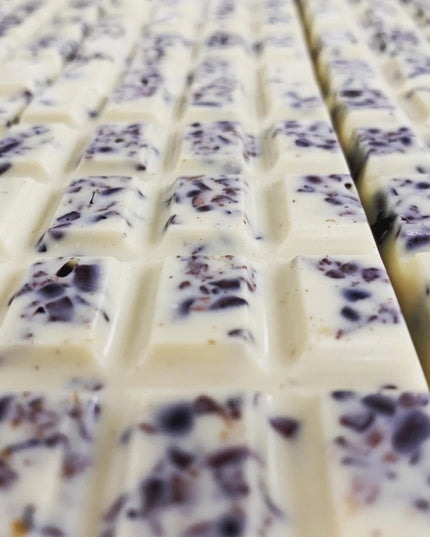 multiple unwrapped chocolate bars tiled next to one another showing the creamy vanilla white chocolate speckled with dark spots of cacao nibs