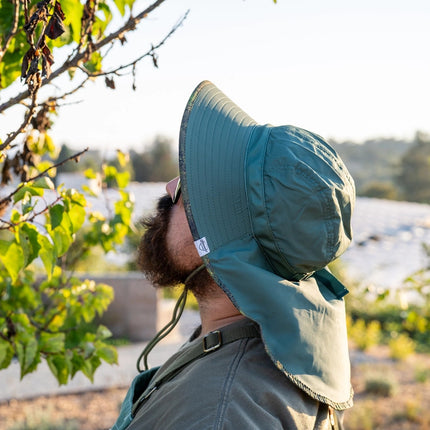 a model facing away from the viewer and wearing the Green Brush Camo Sun Hat with the neck flap covering their neck and upper back