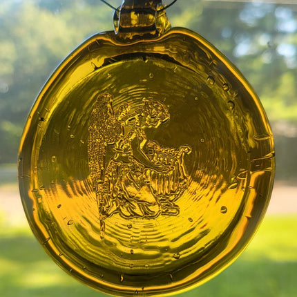 Glass suncatcher, yellow in color, features and angle playing a harp.