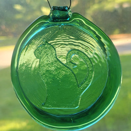 Green glass suncatcher with a sitting cat design. The background is foliage.